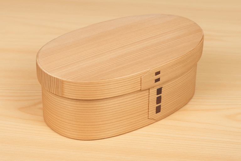 A traditional Japanese magewappa bento box made from natural wood, resting on a smooth wooden surface with visible grain.